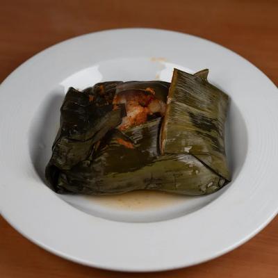 Tamal stuffed with filling and wrapped in a banana leaf.