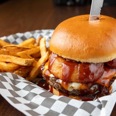 Western burger with onion rings, BBQ sauce, bacon crumble, and cheese, served with fries.