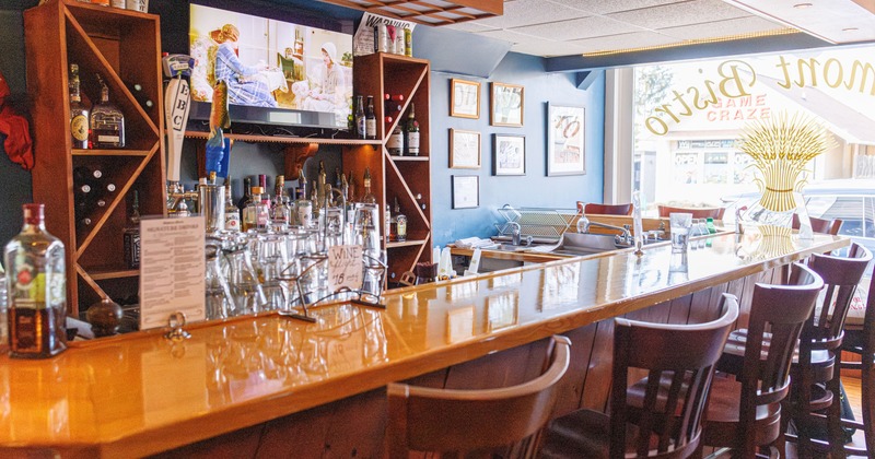 Restaurant interior with wooden bar and high chairs, shelves stocked with drinks and TV