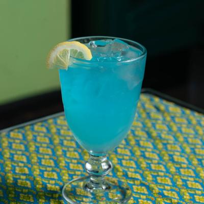 A blue cocktail with ice and lemon garnish on a table.