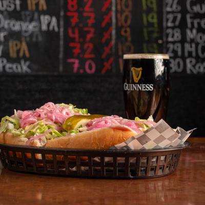 Deli Sub sandwich topped with pink onions and lettuce, served with a beer.