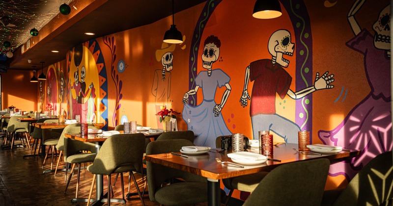 A restaurant interior with tables and a colorful skeleton mural on the wall