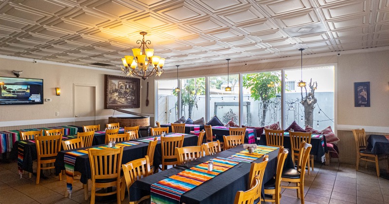 Restaurant dining area with tables, chairs, chandeliers, and large windows