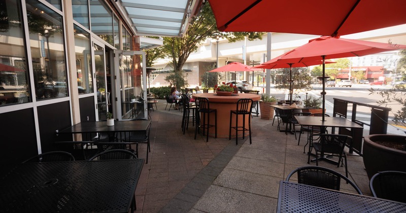Outdoor seating area, black metal tables, red umbrellas, and a central bar table