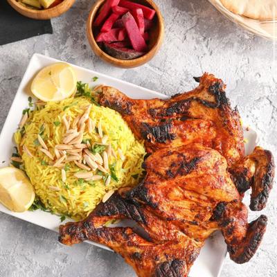 Whole grilled chicken with yellow rice, served with lemon wedges, pickles, beets, and pita bread.