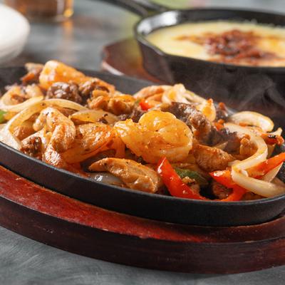 Steaming fajitas with shrimp, meat, peppers, and onions.