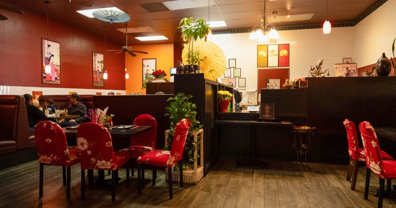 Interior, red and orange walls, decorated with Asian-themed art, paper umbrellas, red floral chairs
