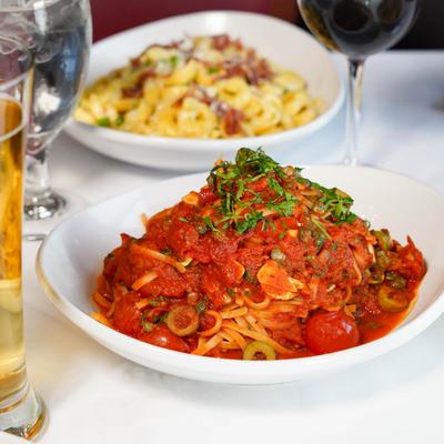 Linguine Puttanesca, a glass of beer and tortellini pasta in the background.