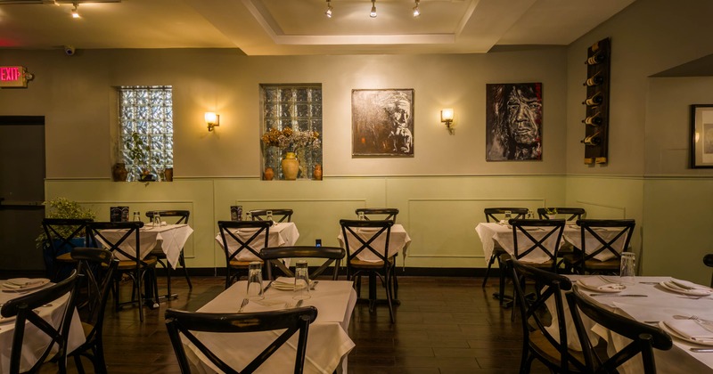 Interior, dining room with white-tablecloth tables, black chairs and artwork