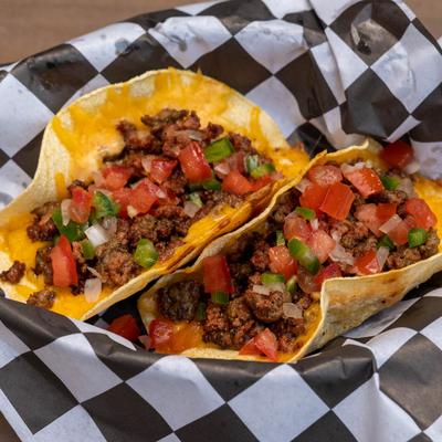 Two tacos filled with seasoned beef, melted cheese, diced tomatoes, onions, and bell peppers.