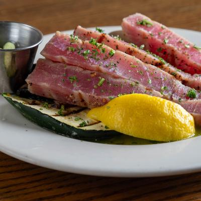 Grilled and sliced rare tuna steaks served with grilled vegetables and a lemon wedge.