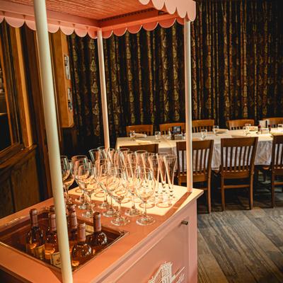 Pink cart with wine glasses and bottles with a table set for guests.