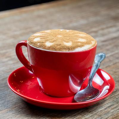 Cappuccino topped with cinnamon powder, served in a red cup on a matching saucer.