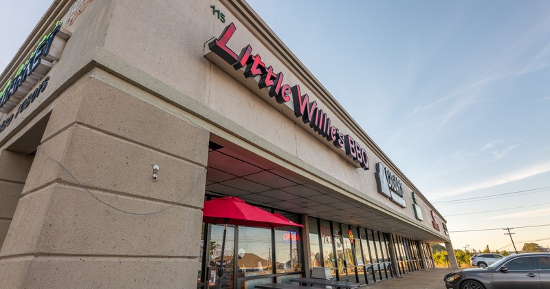 Exterior, angle view to restaurant and sidewalk patio, tables, chairs, parasols, sign above entrance
