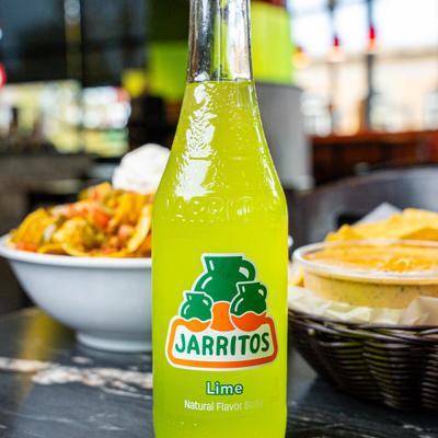 A bottle of Mexican flavor soda on a table, with food in the background.