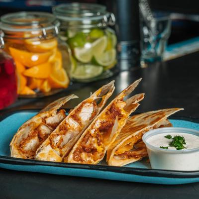 Chicken quesadilla wedges served with a cup of dipping sauce.