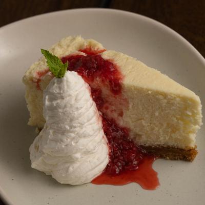 A slice of cheesecake with whipped cream and raspberry sauce.