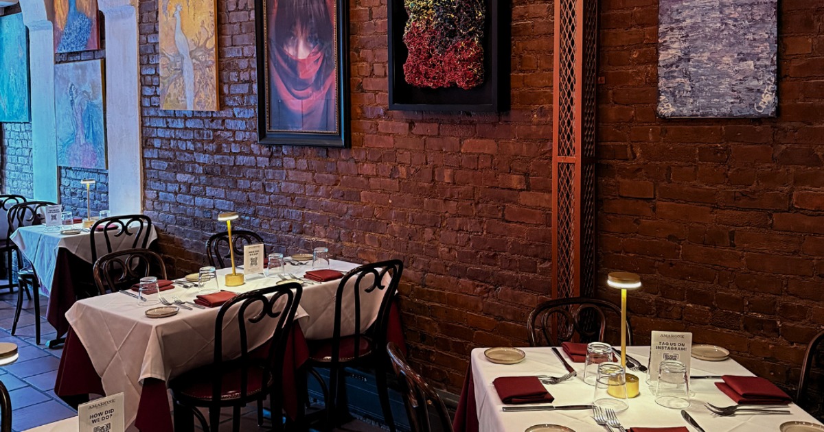 Restaurant dining room featuring set tables along a brick wall with framed art