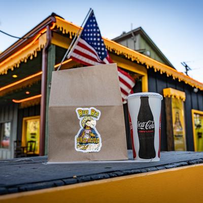 A takeout bag and a soda cup in front of a building with an American flag.