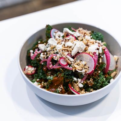 A white bowl of kale salad with radishes, quinoa, feta cheese, and pickled onions.