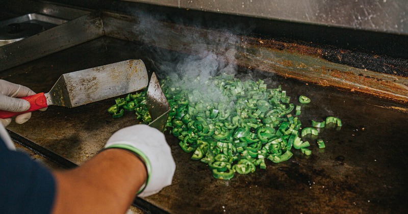 A cook grilling fresh green peppers