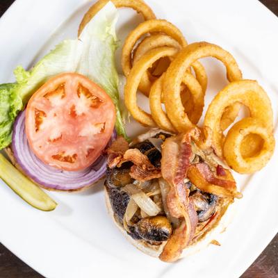 Burger topped with mushrooms, onion, bacon and fresh vegetables, served with onion rings.