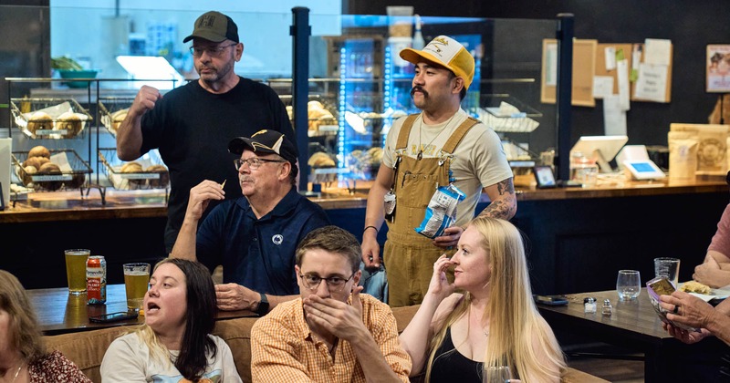 Group of people engrossed in conversation or an event, pastries and snacks visible in the background