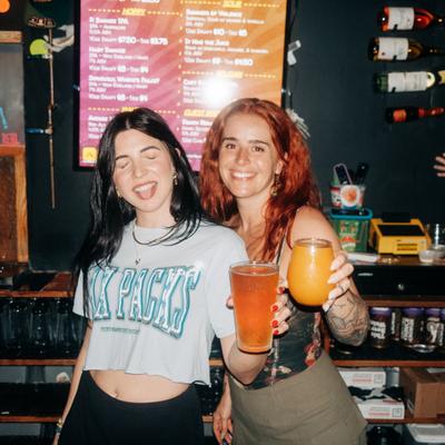 Two people holding drinks inside a bar.