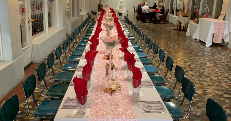 A long table with red napkins, glasses, flowers and place settings