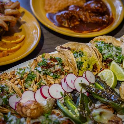 Assorted tacos with other Mexican dishes in the background.