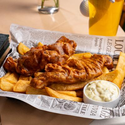 Fish and Chips served in a basket lined with paper with a side of tartar sauce.