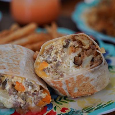 A close-up of a halved burrito and fries on a decorative plate.