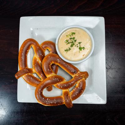 Two salted pretzels served with a creamy cheese dip.