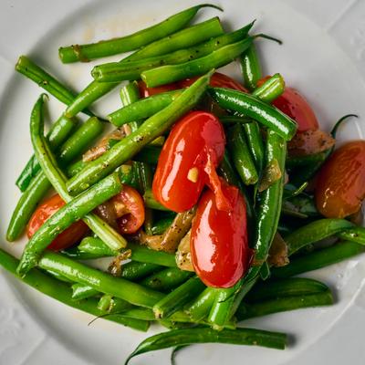 Green beans and tomatoes on a white plate.