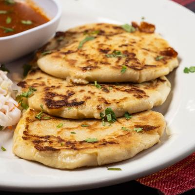 Grilled stuffed tortillas sprinkled with herbs beside slaw and salsa, close up.