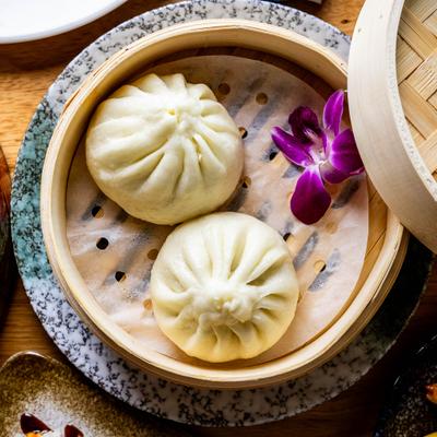 Two steamed buns in a bamboo steamer, decorated with a purple orchid.