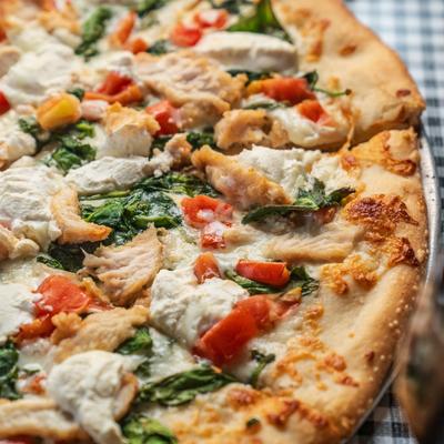 Close-up of a pizza topped with chicken, spinach, tomatoes, and ricotta  cheese.
