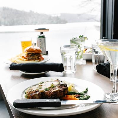 Dry Rubbed Pork Porterhouse, burger, drinks, and a Martini on table by a window.