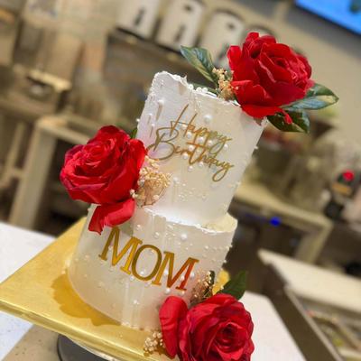 Two-tier white frosted birthday cake decorated with pearls, and red roses.