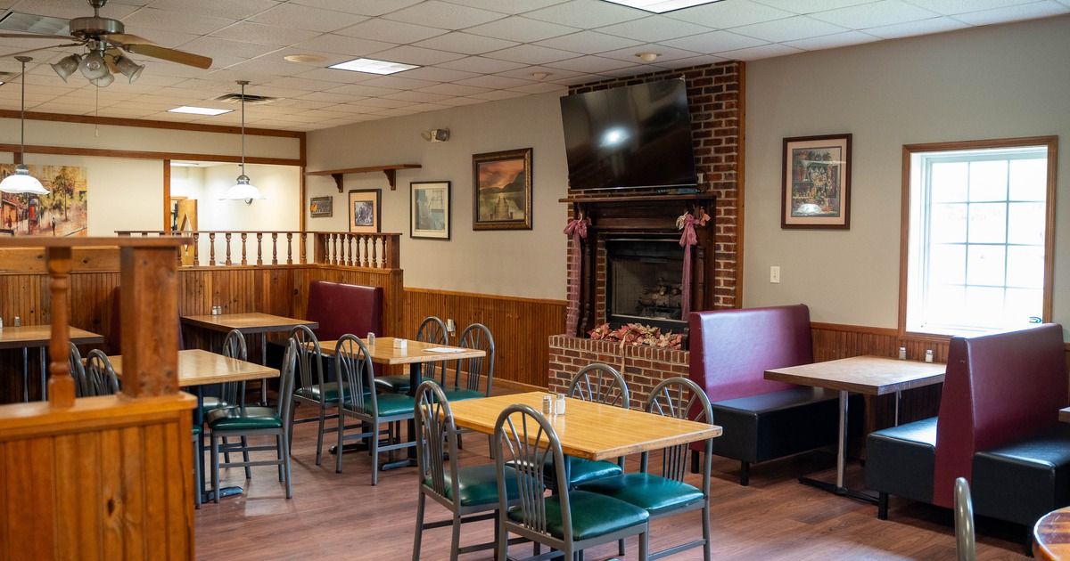 Interior - wooden tables, green chairs, burgundy booths, a brick fireplace with a TV above.