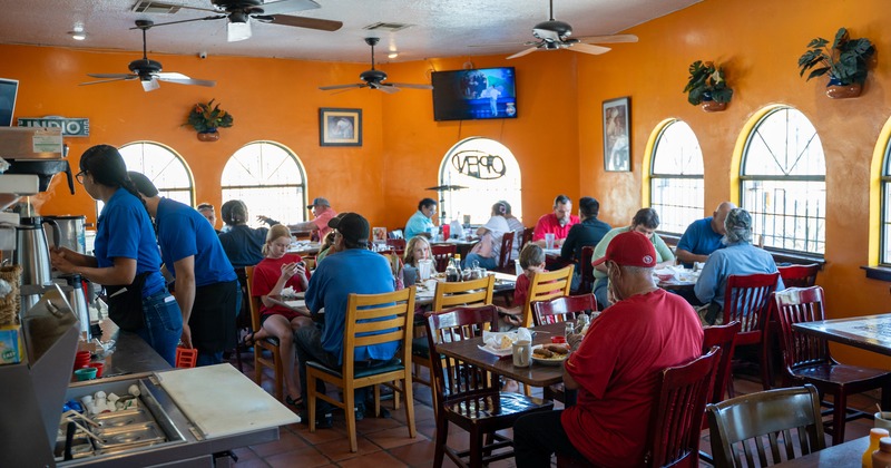 Diner area, tables, chairs, fool of people, tv screen above