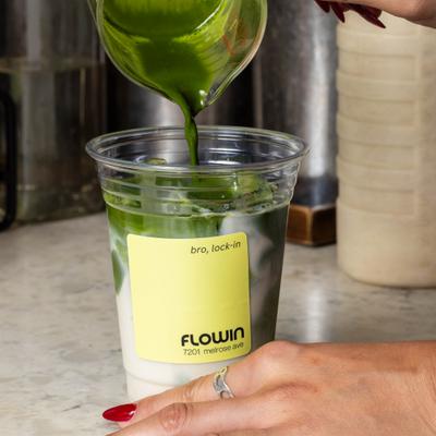 Matcha drink being poured from a glass spout into a plastic cup with ice.