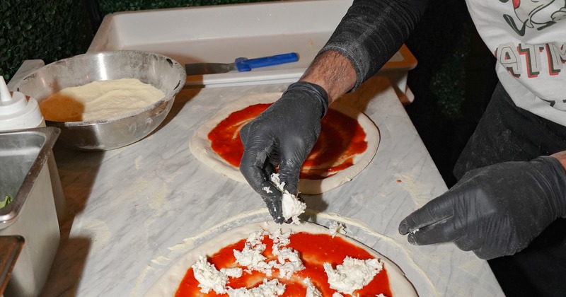 Adding cheese to pizza topped with tomato sauce, hand shot