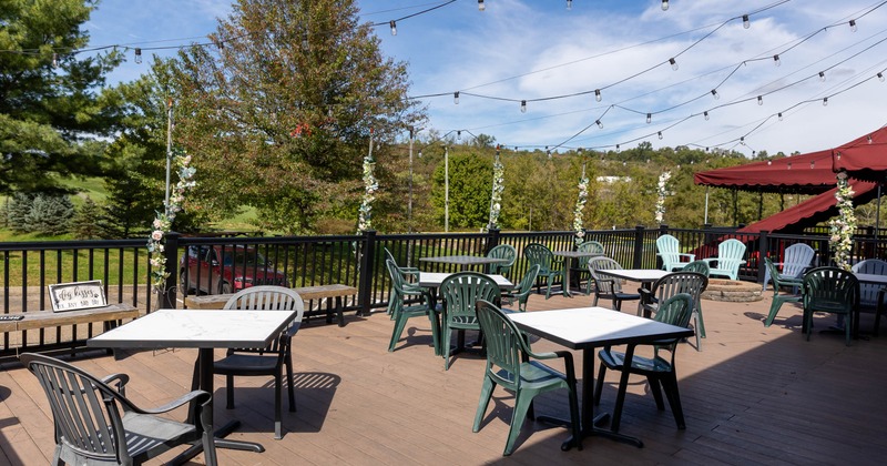 Outdoor deck with patio tables, string lights, and scenic greenery