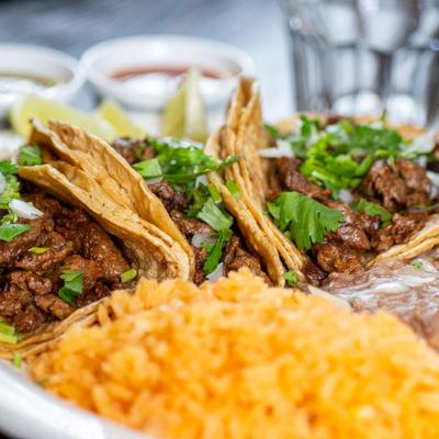 Close-up of beef tacos topped with cilantro and onions, served with rice and beans.