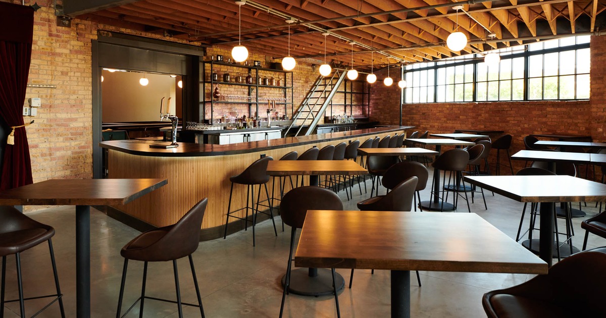Modern industrial bar with wooden tables, dark chairs, and pendant lights