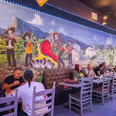 Mexican restaurant interior with a mariachi skeleton mural and guests seated at tables.