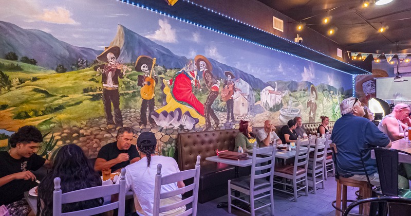 Mexican restaurant interior with a mariachi skeleton mural and guests seated at tables
