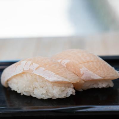 Yellowtail nigiri served on a dark plate.
