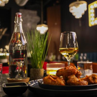 Plate of crispy fried chicken served alongside wine, bottle of water and a potted plant.